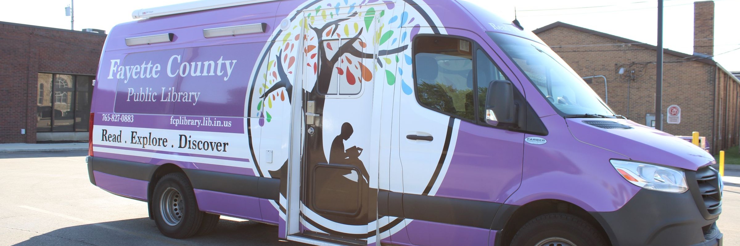 Purple Fayette County Library sprinter van with large rainbow tree and reader logo icon in white circle on the side